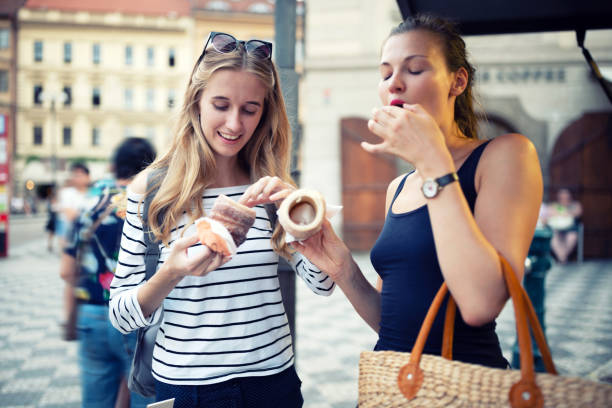 Young women go shopping in the city and eating Trdelnik (traditional Czech hot sweet pastry) Young women go shopping in the city and eating Trdelnik (traditional Czech hot sweet pastry) trdelník stock pictures, royalty-free photos & images