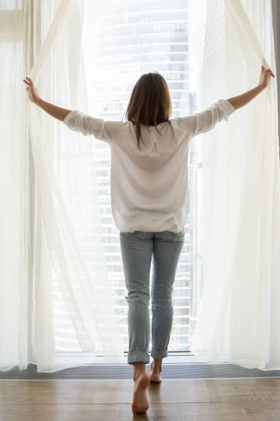 Happy woman opening curtains enjoying view from window