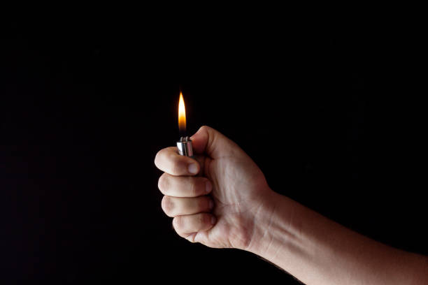 Cropped Hand Of Woman Igniting Cigarette Lighter Against Black Background  cigarette lighter stock pictures, royalty-free photos & images