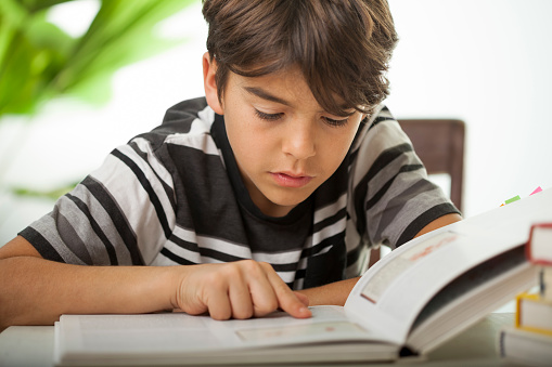 a concentrated boy reading a large book indoors