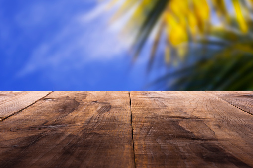 Pine wood table with defocused palm tree leaf and blue sky