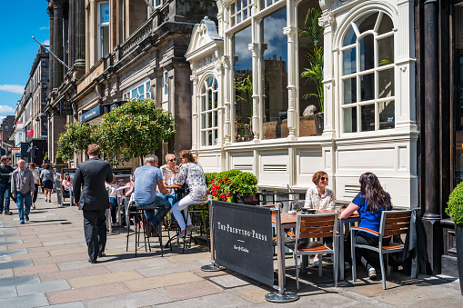People enjoy a restaurant patio in downtown in Edinburgh, Scotland, UK on a sunny day.