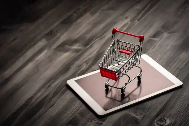 close-up of shopping trolley on tablet with darkwood background with some copy space,shopping online concept.