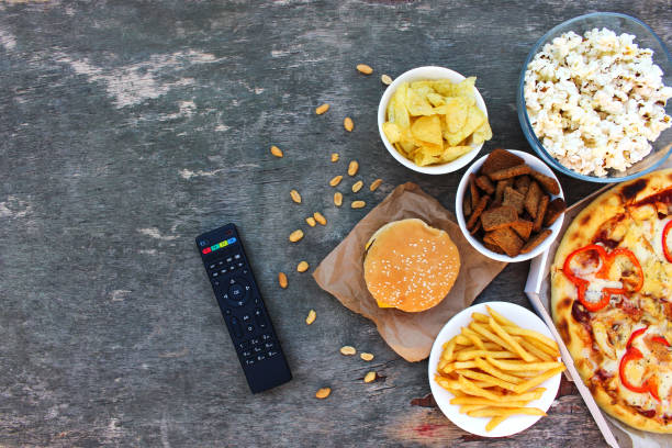 TV remote control, fast food on old wooden background. Concept of junk eating. Top view. Flat lay. TV remote control, fast food on old wooden background. Concept of junk eating. Top view. Flat lay. remote control on table stock pictures, royalty-free photos & images