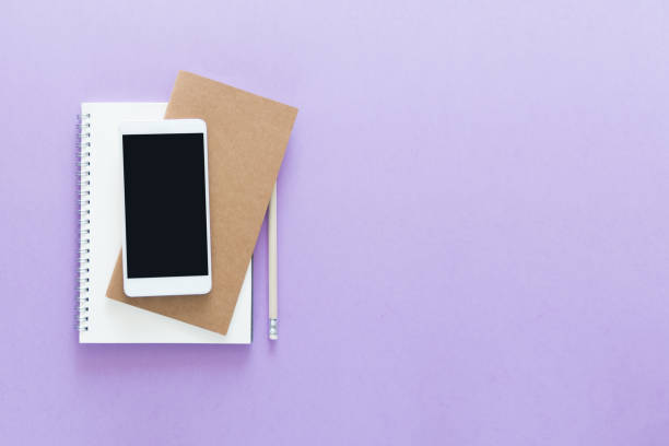 istock Top view over the working desk with opened notebooks and phone at the top. Copy space for text. Flat lay of a workplace on violet background 1032451886