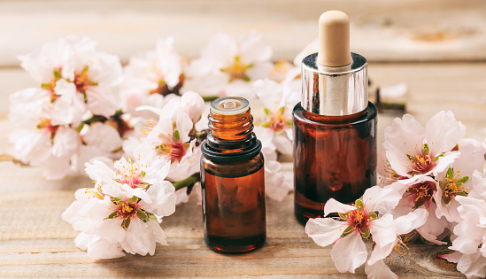 Natural cosmetics. Pink almond blossoms and essential oil containers on wooden table