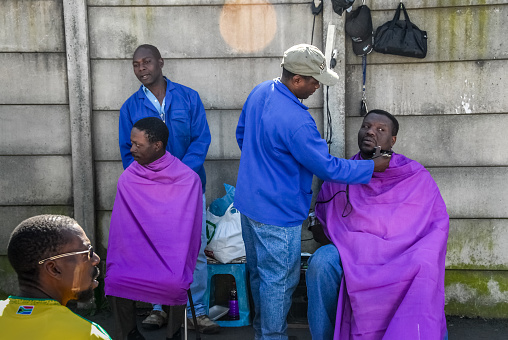 Johannesburg , Gauteng / South Africa -august 31 2012 : two men getting their hair cut and trimmed on a sidewalk  midday Rosettenville Johannesburg