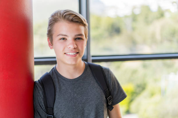 Smiling male student leaning on column in school