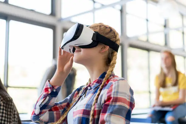 Teenage student wearing virtual reality glasses in classroom. Girl is using technology while studying. She is in high school.