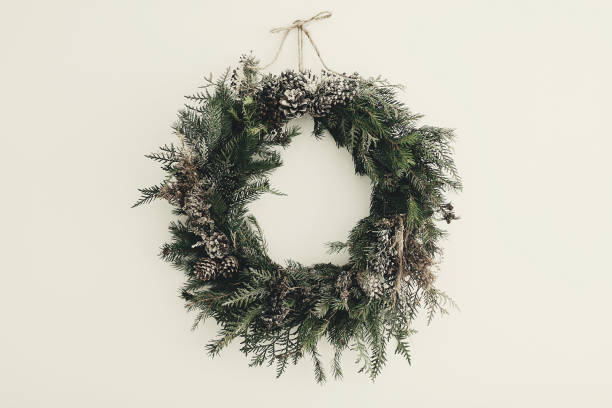 modern Christmas wreath. stylish rustic christmas wreath with pine cones,fir branches,snow, hanging on white wall. space for text. handmade decor for winter holidays stock photo