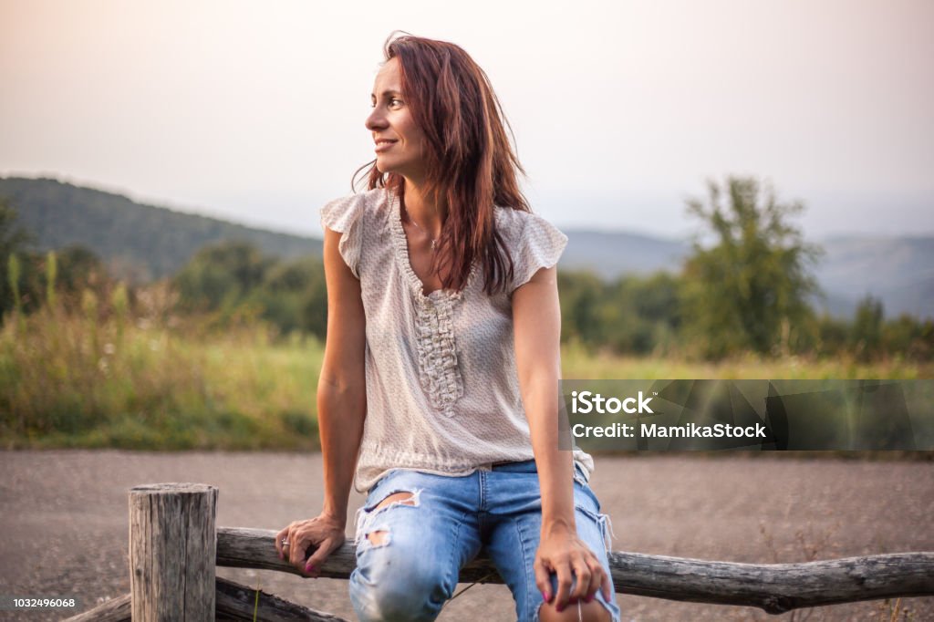 Profil d’une femme d’âge mûr assis sur une barrière en bois dans la nature - Photo de Femmes libre de droits