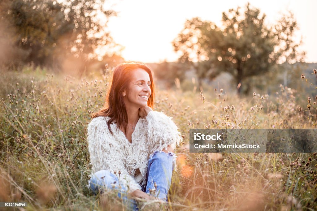 Portrait of a mature woman in park Beautiful woman sitting in the field enjoying the sunset Women Stock Photo