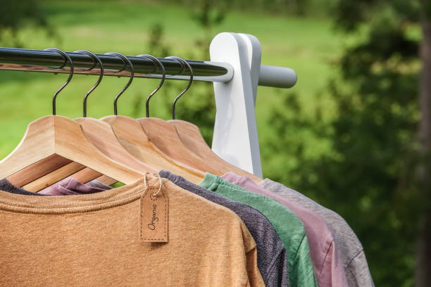 Organic clothes, t-shirts hanging on wooden hangers with green forest, nature in background. stock photo