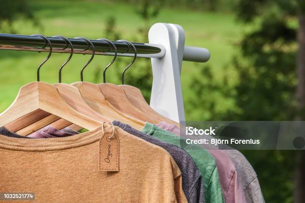 Organic Clothes Tshirts Hanging On Wooden Hangers With Green Forest Nature In Background Stock Photo - Download Image Now