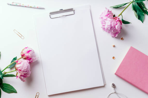 istock Feminine workspace with empty paper and pink peons on white background with copy space 1032528066