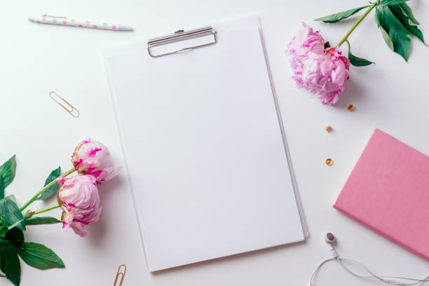 istock Feminine workspace with empty paper and pink peons on white background with copy space 1032528092