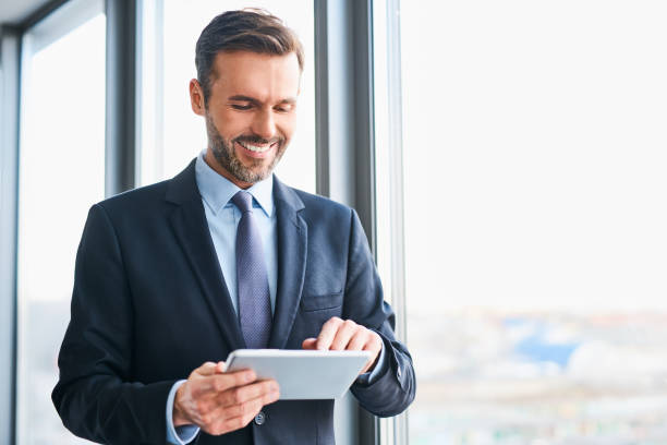 heureux homme d’affaires à l’aide de tablette numérique permanent au bureau - standing digital tablet adult beautiful photos et images de collection