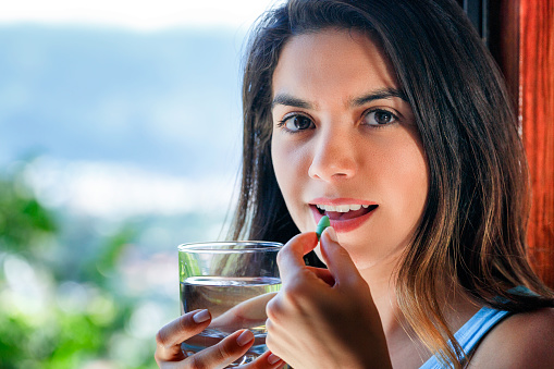 Health themes. Close-up of Hispanic young woman ready taking pill with glass of water in hand