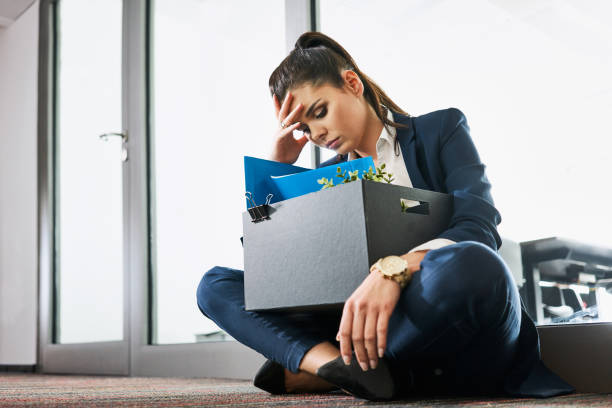 Fired young woman, employee sitting with box outside the office stock photo