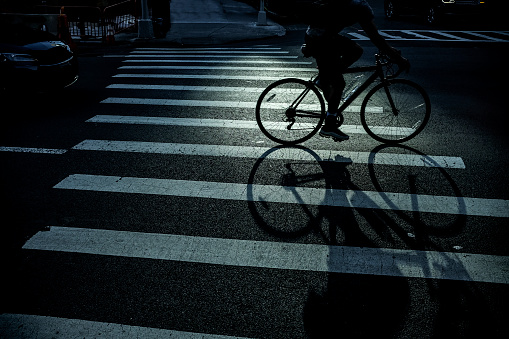 Long shadow of man riding bicycle over crosswalk