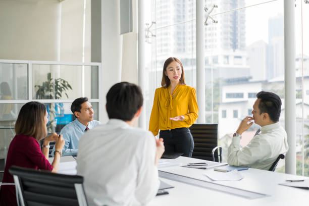 Businesswoman giving presentation in board room Confident businesswoman giving presentation in board room. Professionals are in meeting at conference table. They are sharing ideas in office. malaysia office workers stock pictures, royalty-free photos & images