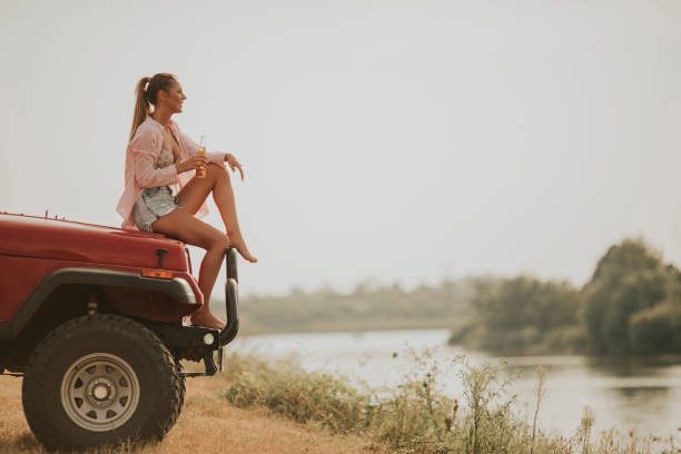 istock Young woman sits on a car hood and drinks refreshment 1032553118
