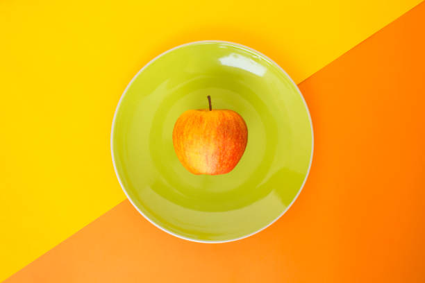istock red apple green plate on orange and yellow background 1032560624
