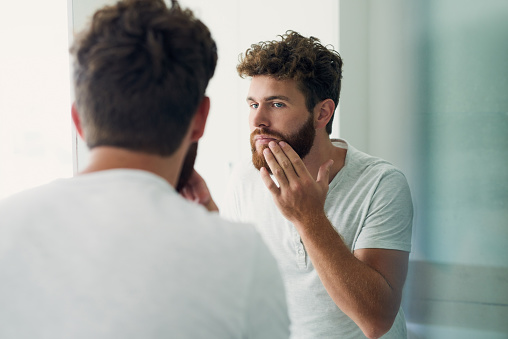 Cropped shot of a handsome young man checking out his skin in the bathroom mirror