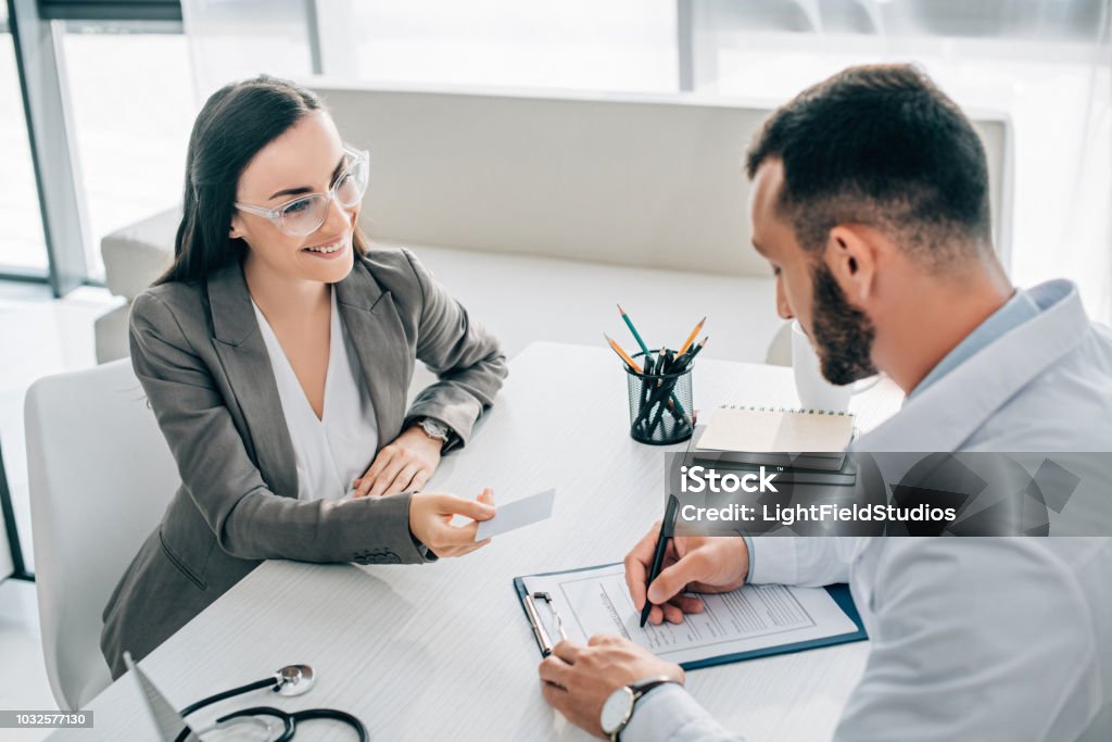 high angle view of smiling patient giving id card to doctor to fill insurance claim form in hospital Claim Form Stock Photo