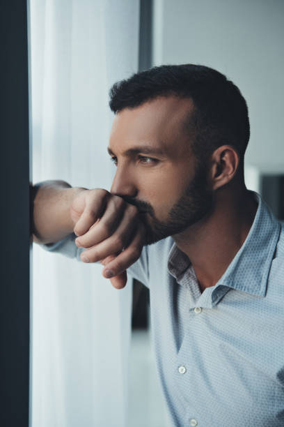 istock thoughtful man standing at window at home 1032581214