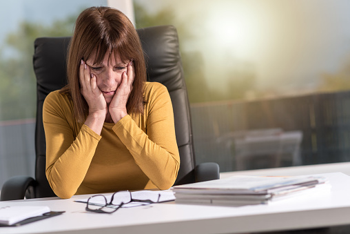 Desperate businesswoman with head in hands sitting at desk, light effect