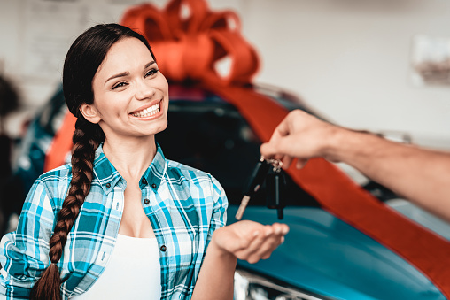 A Guy Gives A Car Key To Girlfriend. Present Concept. Automobile Salon. Make A Decision. Gift Ribbon. End Of A Deal. Good Offer. Happy Together. Successful Buying. Beautiful Surprise.