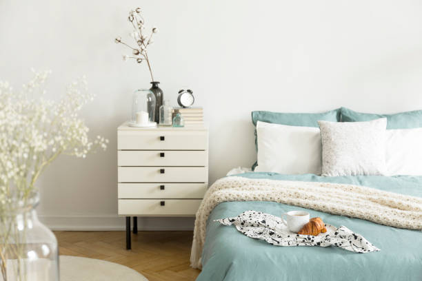 istock A bright bedroom interior with sage green and white bedding, pillows on bed and a drawer nightstand. Real photo. 1032584776