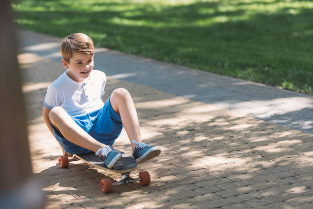 istock high angle view of cute smiling boy sitting on skateboard in park 1032585706