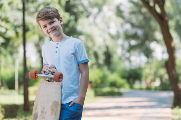 istock happy kid standing with skateboard and smiling at camera in park 1032585740