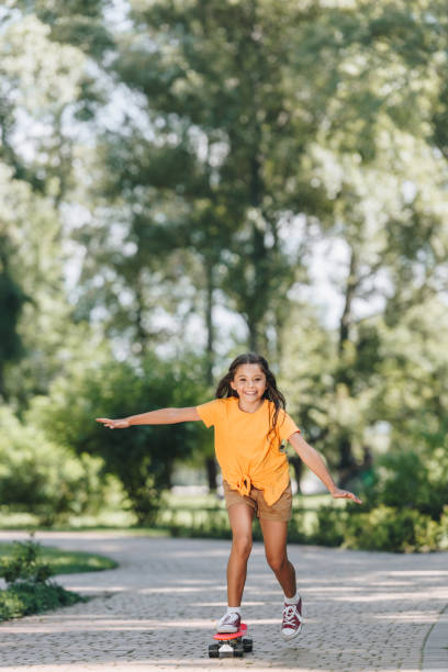 istock cute happy child riding skateboard and smiling at camera in park 1032585752