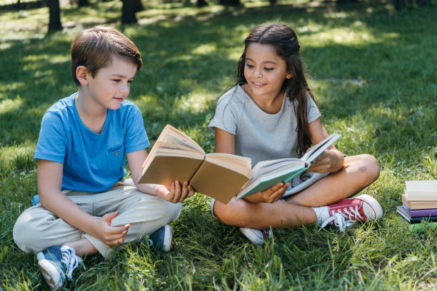 istock cute little kids sitting on grass and reading books 1032586374