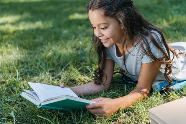 istock cute smiling child lying on grass and reading book 1032586402
