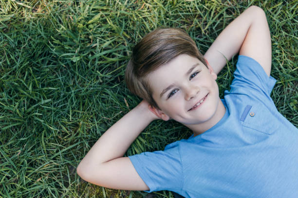 istock top view of happy boy lying with hands behind head on grass and smiling at camera 1032586410