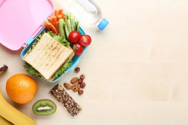 Photo of School lunch box with fruits and vegetables on wooden table