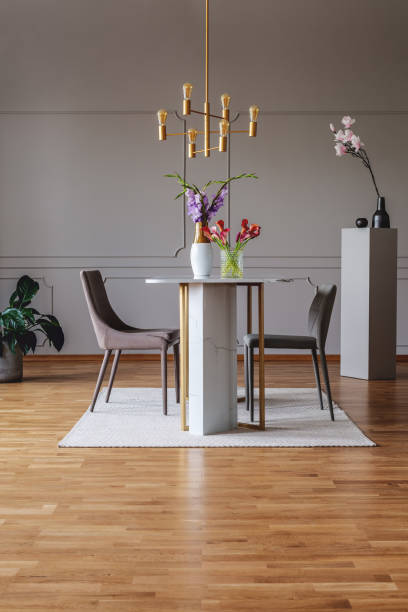 istock Gold lamp above table with flowers in spacious grey dining room interior with chairs. Real photo 1032604164