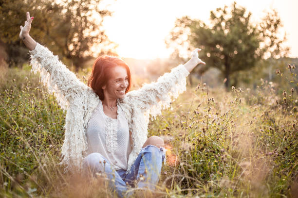 Cheerful mature woman sitting in the field on a sunset