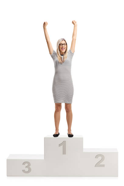 Full length portrait of an overjoyed young woman standing on a winners pedestal isolated on white background