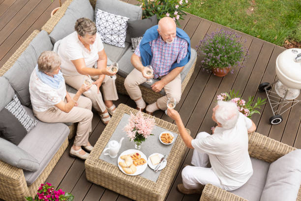Top view of old friends reunion outside on a wooden deck. Happy seniors making a toast during their celebration. Top view of old friends reunion outside on a wooden deck. Happy seniors making a toast during their celebration. drinks on the deck stock pictures, royalty-free photos & images