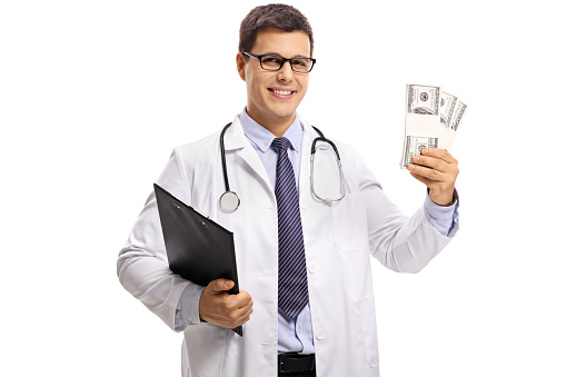 Doctor with a clipboard and bundles of money isolated on white background