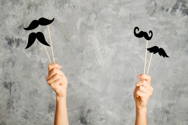 Paper party attributes in form of moustache on wooden stick. Carnival accessory concept. Movember concept. November is month of men health issues and prostate cancer awareness. Young woman holding paper moustache of different style on stick with two hands. Background, close up, copy space women movember mustache facial hair stock pictures, royalty-free photos & images