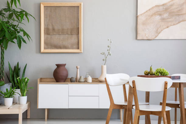 新鮮な果物や 2 つのポスター、緑の植物の装飾と小さな食器棚と明るい灰色部屋インテリアの本物の写真で白い木製の椅子のダイニング テーブル - two pears ストックフォトと画像