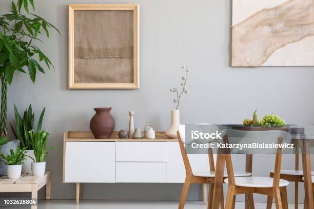 Dining Table With Fresh Fruits And White Wooden Chairs In Real Photo Of Light Grey Room Interior With Two Posters Green Plants And Small Cupboard With Decor Stock Photo - Download Image Now