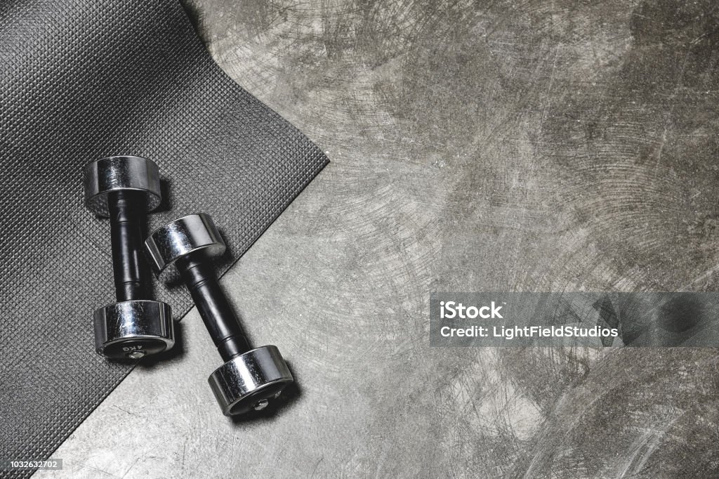 top view of yoga mat and dumbbells lying on concrete surface Dumbbell Stock Photo