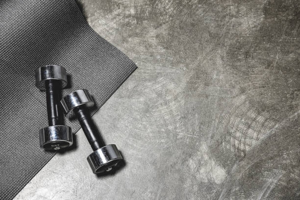 top view of yoga mat and dumbbells lying on concrete surface top view of yoga mat and dumbbells lying on concrete surface exercise equipment stock pictures, royalty-free photos & images